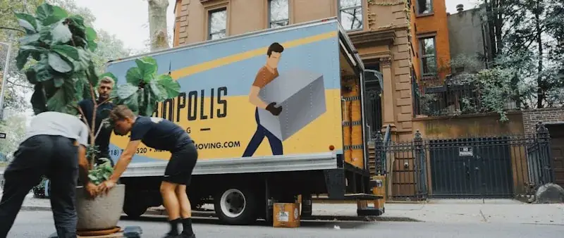 Two professional movers in orange safety vests loading wooden furniture into white utility truck for removals and moving service in Melbourne